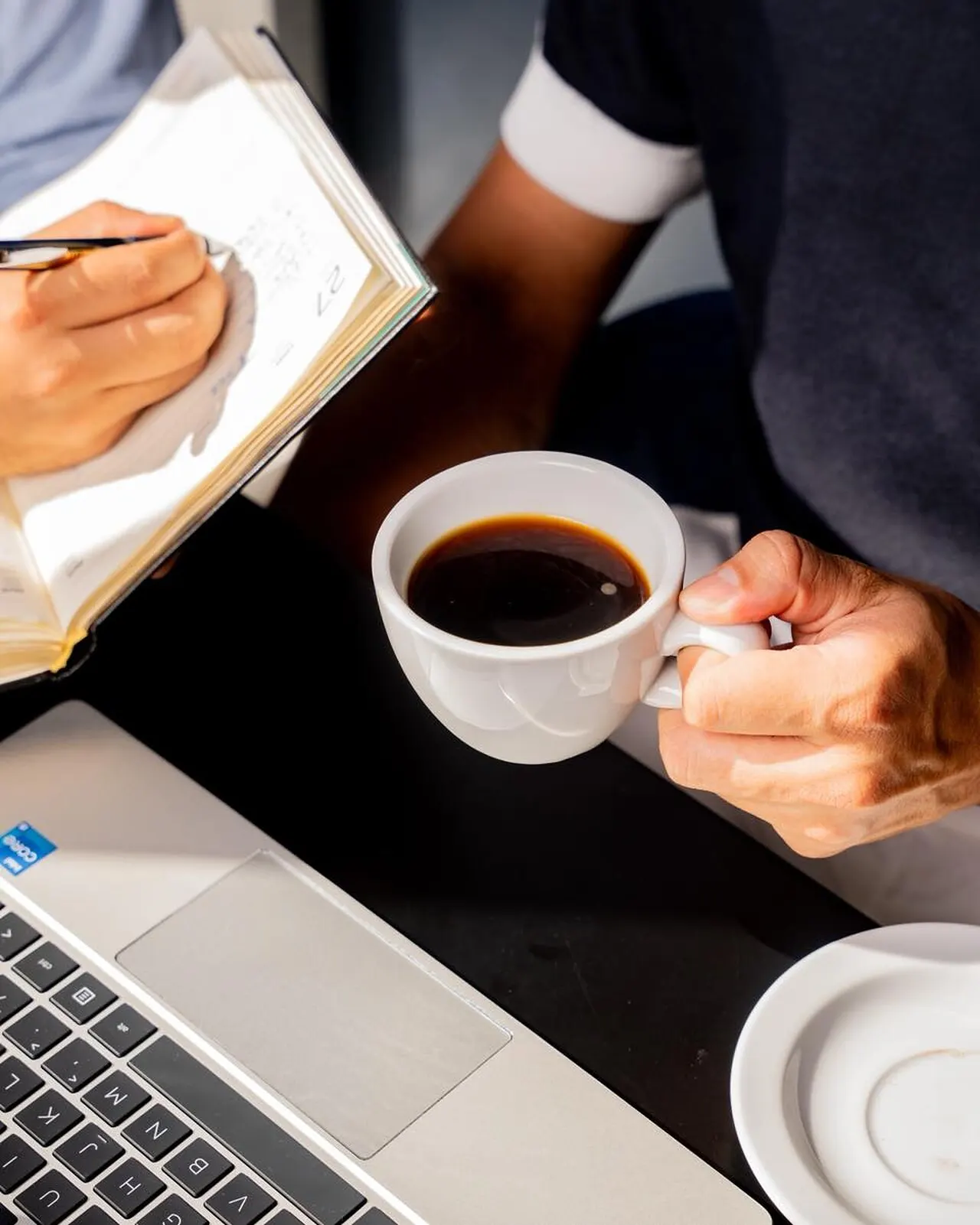 Taza de café negro sobre una laptop, junto a una libreta