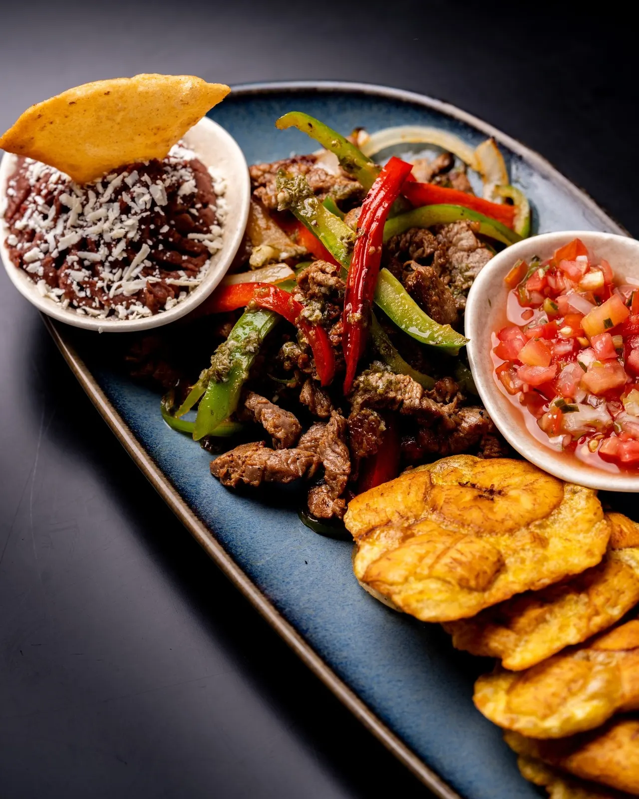 Tostones con carne salteada, pico de gallo y frijoles molidos en un plato azul